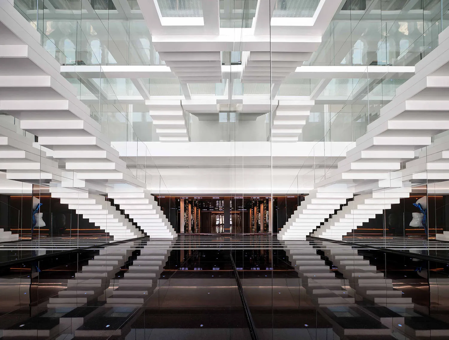 A modern office lobby with glass staircases and a reflective floor.