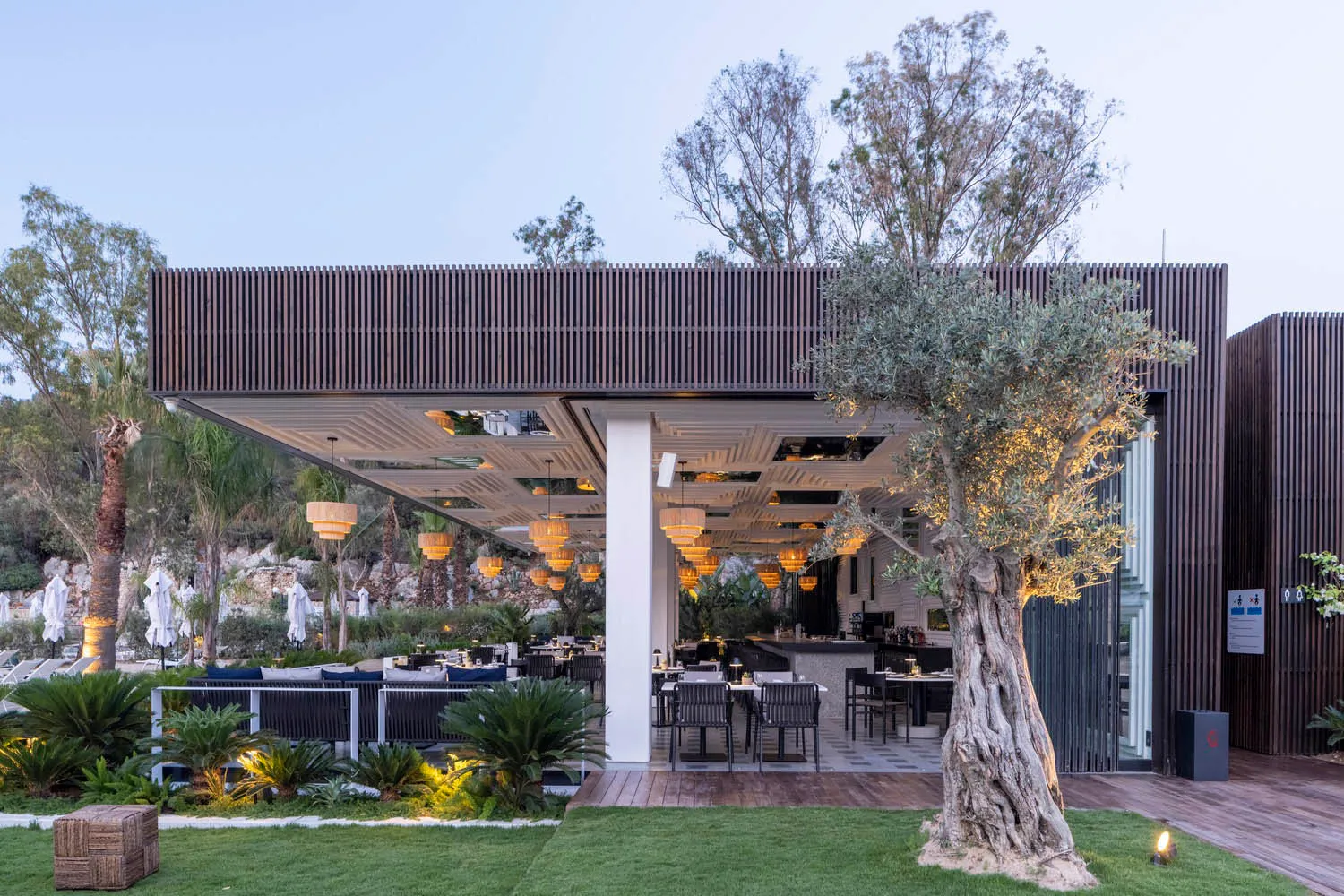 A modern outdoor restaurant with wooden panels, trees, and large windows overlooking a natural landscape.