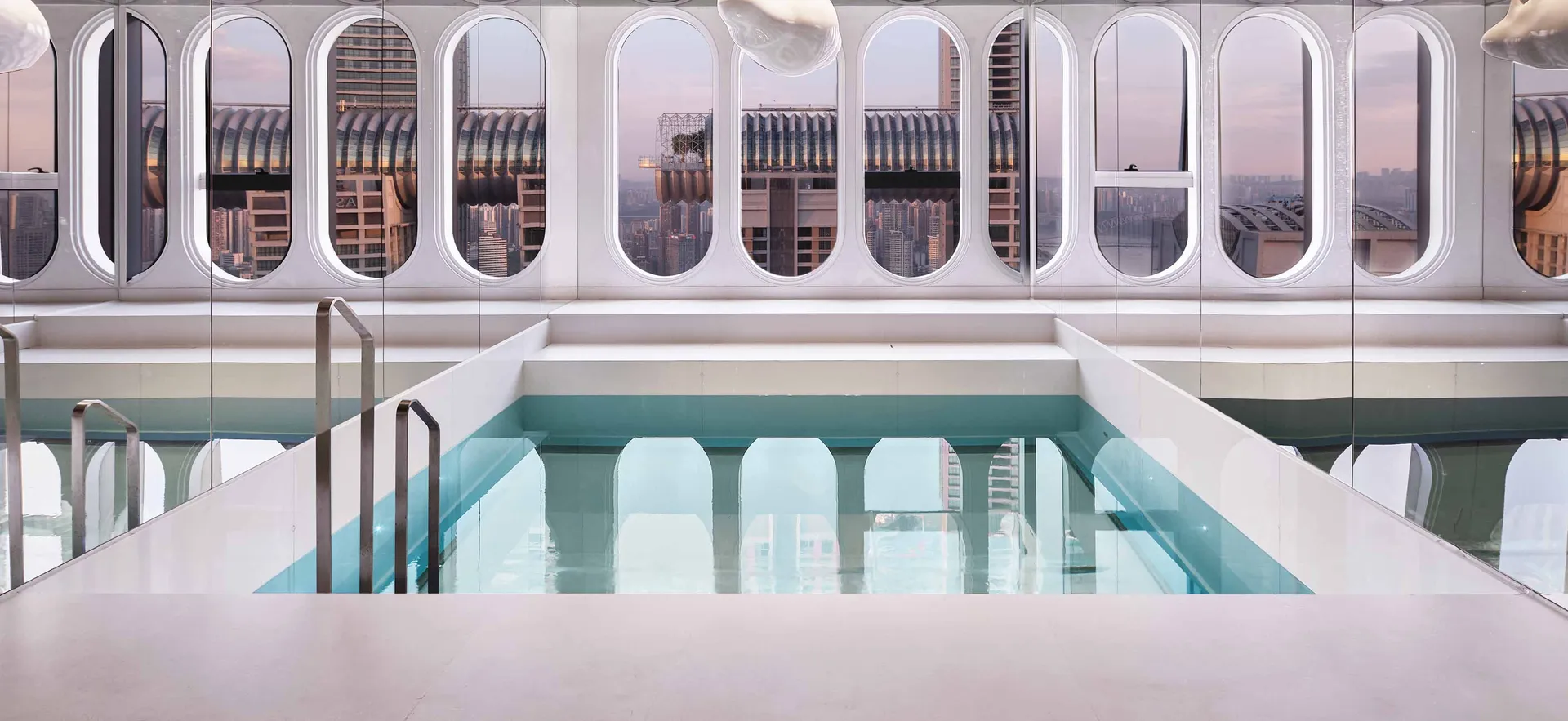 Modern rooftop swimming pool enclosed by a glass fence overlooking a cityscape.