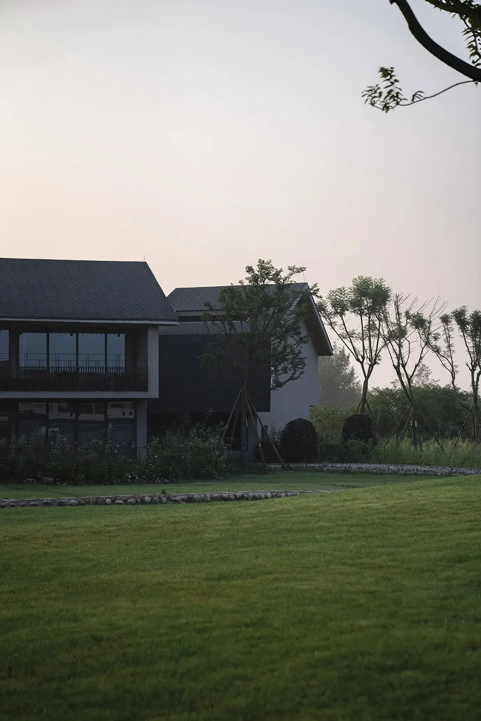 A modern house with concrete and glass exterior surrounded by greenery.