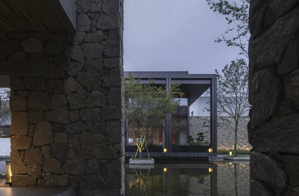 Modern exterior of a residential house featuring stone walls, a glass wall, and a landscaped garden.