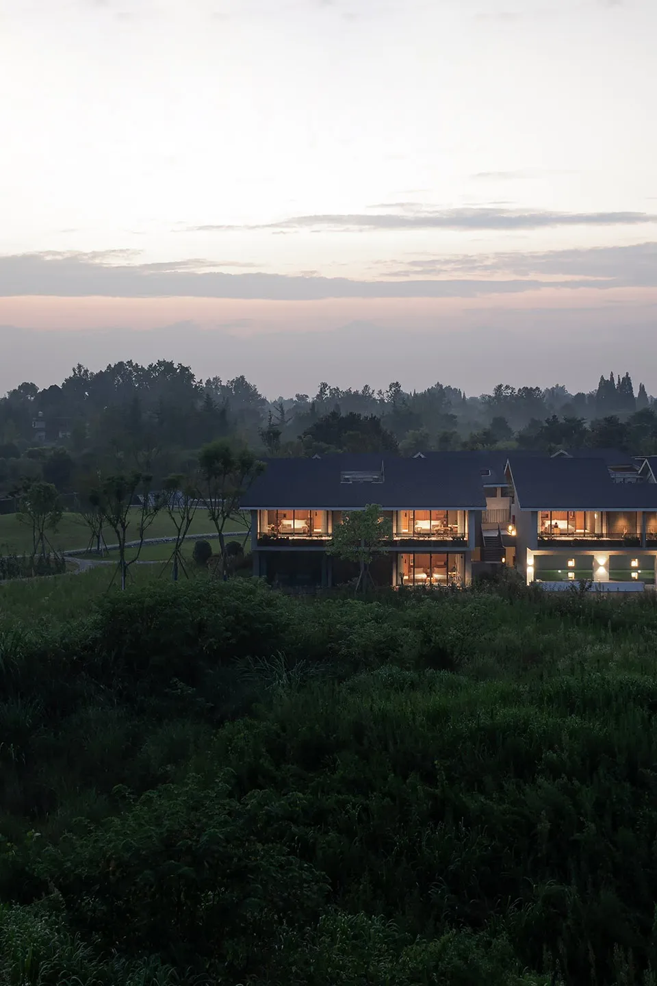 A modern residential home with glass windows and a garden view at sunset.