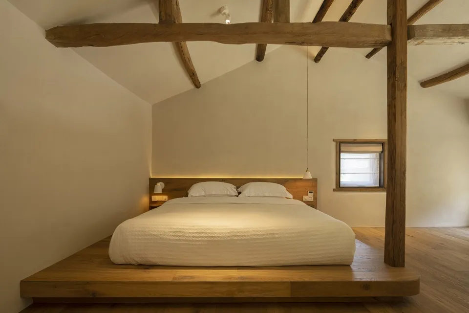 A minimalist bedroom featuring a wooden platform bed with white bedding and a window