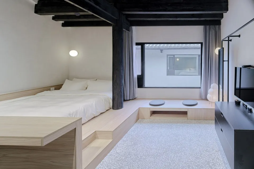 Minimalist bedroom with wood floor, stone accent, and large window.