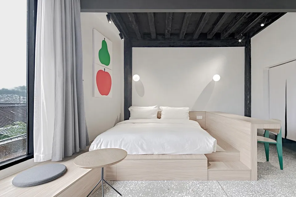 A minimalist bedroom with a bed on a raised platform made of white terrazzo and wood