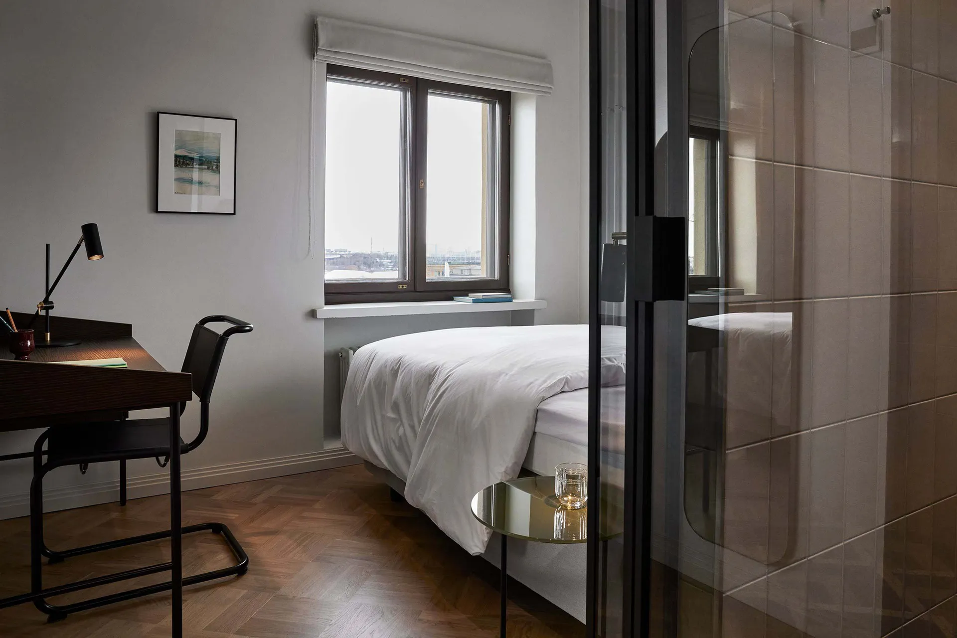 A minimalist bedroom with a white bed, a desk, and a glass door.