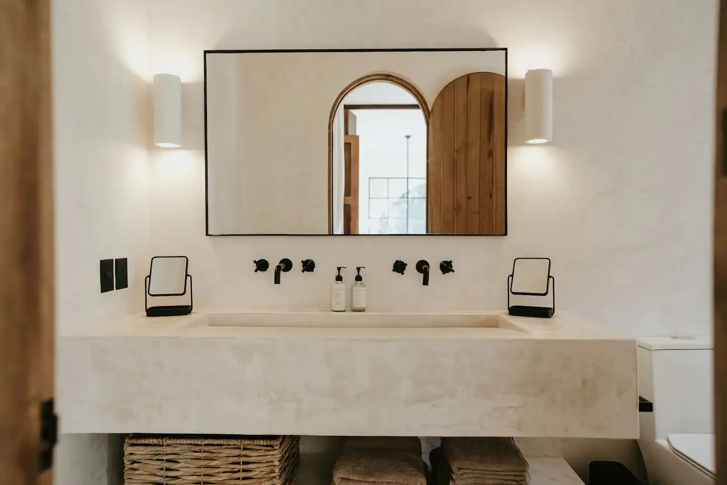 A modern bathroom with a concrete sink, black faucets, and a wooden door.