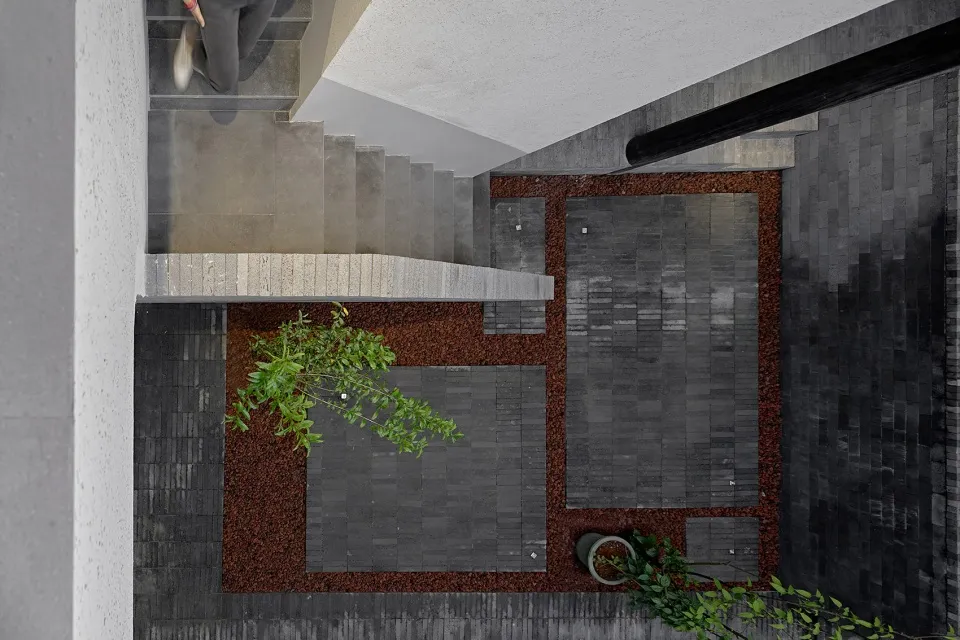 A modern interior space with concrete flooring and wooden stairs adjacent to a patio covered in dark soil with a single plant