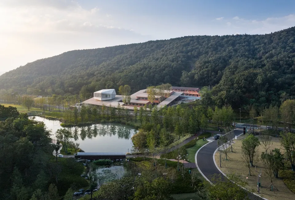 A serene landscape featuring concrete structures amidst lush greenery and a serene pond, surrounded by rolling hills.