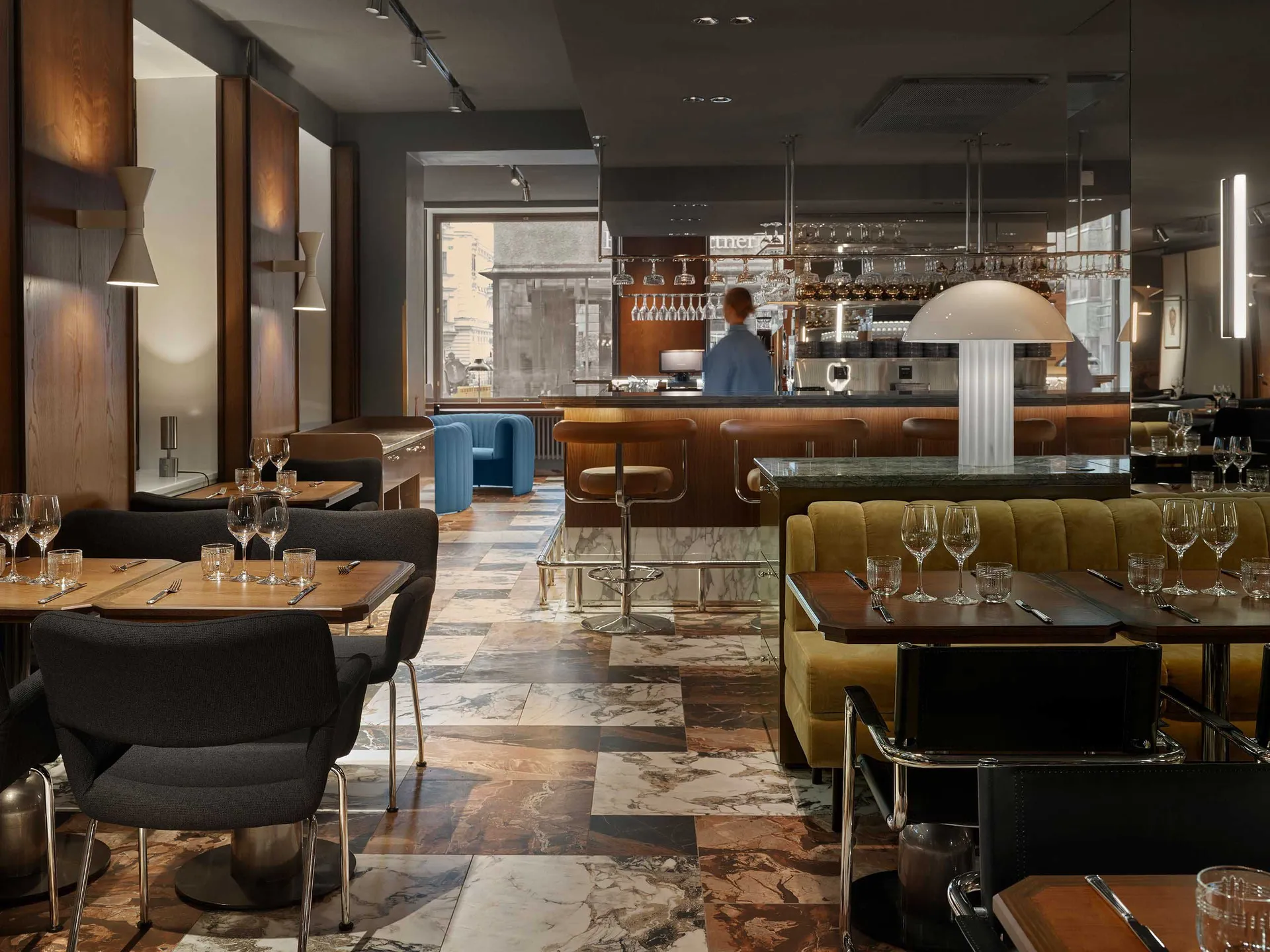 Modern restaurant bar with marble countertops, leather seating, and wooden tables and chairs.