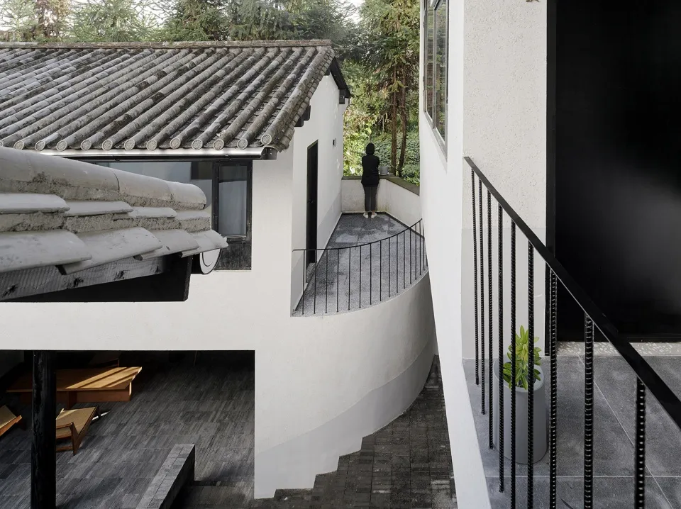 A modern house with white walls and concrete roof tiles, featuring a curved balcony.