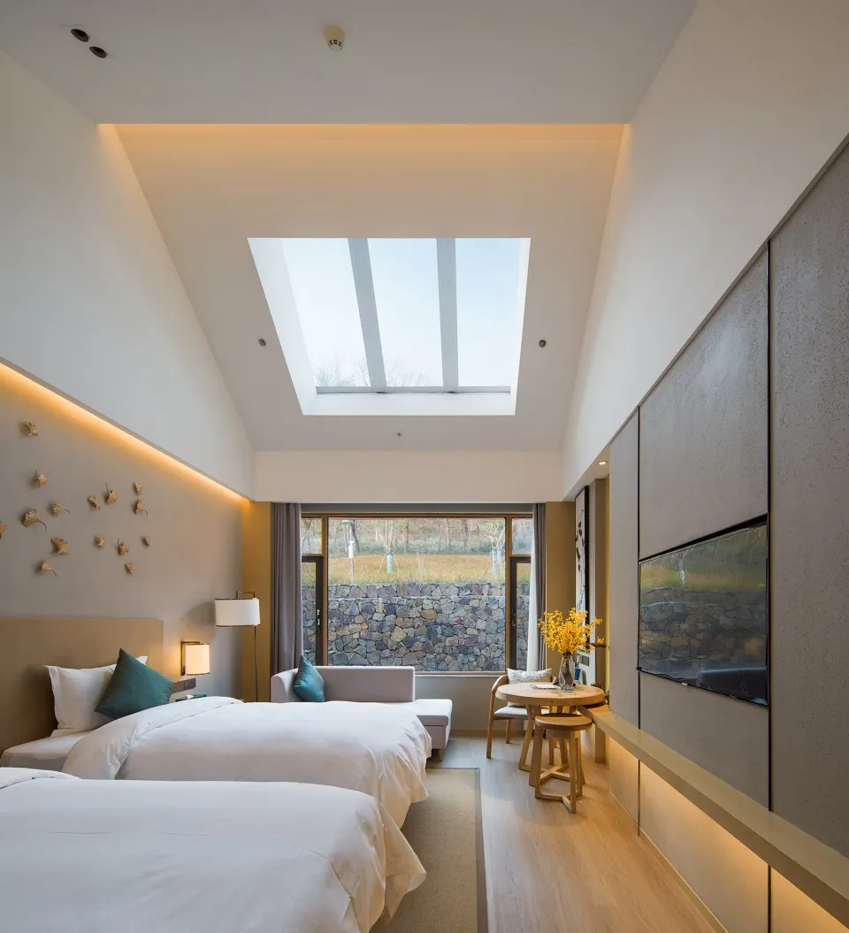 A modern minimalist bedroom with neutral-toned walls and furniture, featuring two twin beds, a double-height ceiling with a s