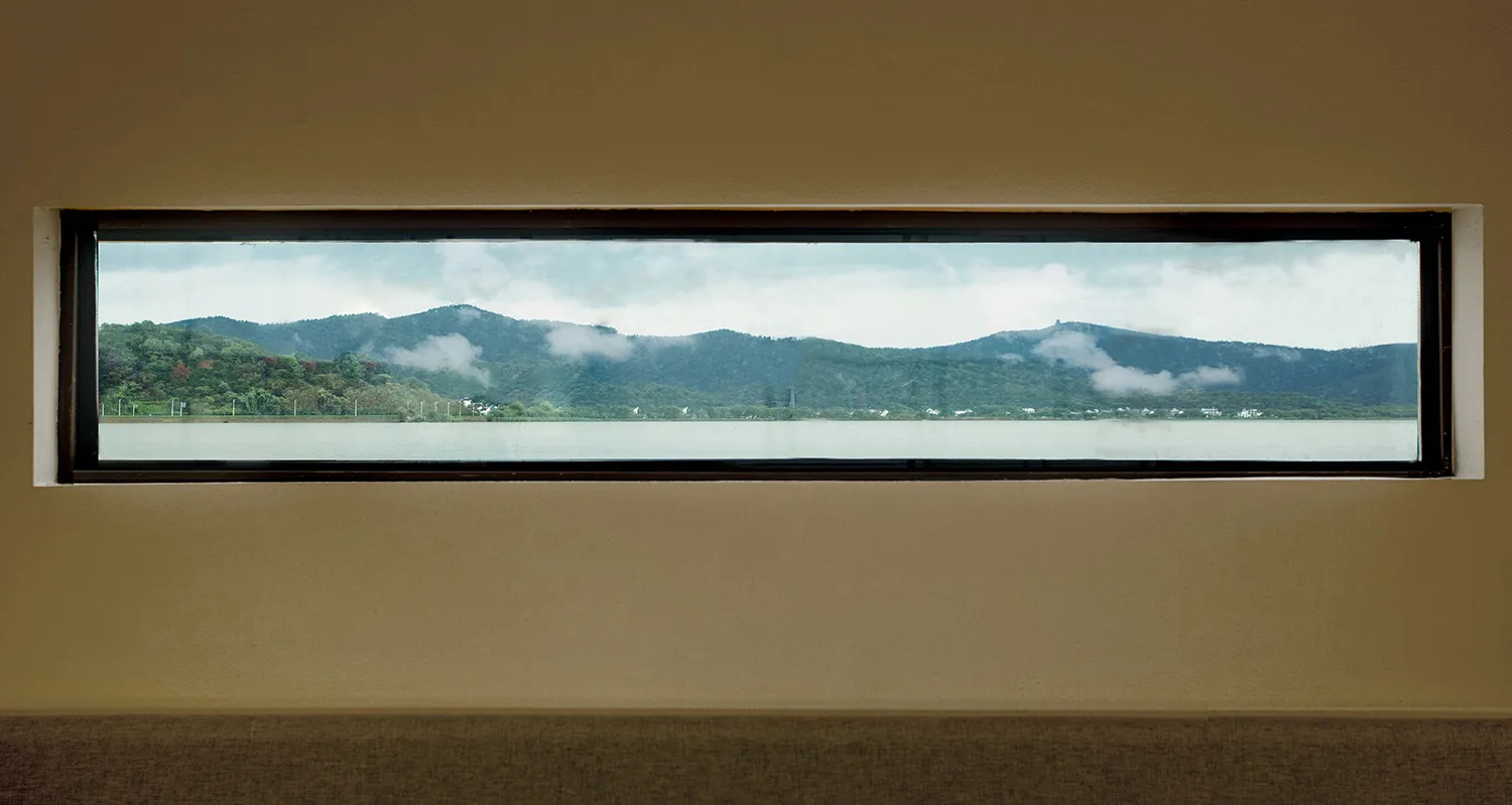 A rectangular window overlooking a serene lake surrounded by mountains and clouds in the background.