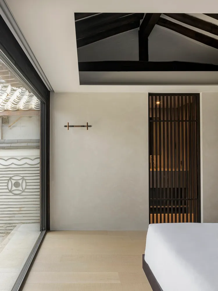 A minimalist bedroom with wooden flooring, a bed, and a simple white wall with a wooden door.