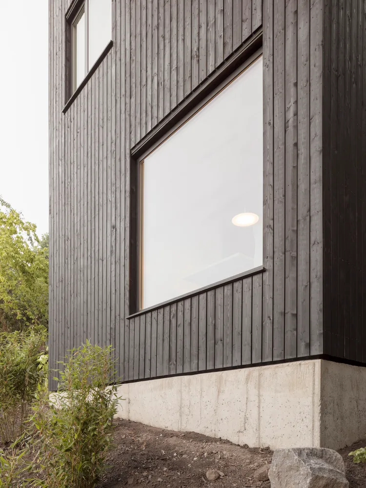 Modern black wooden exterior house with large windows and concrete foundation