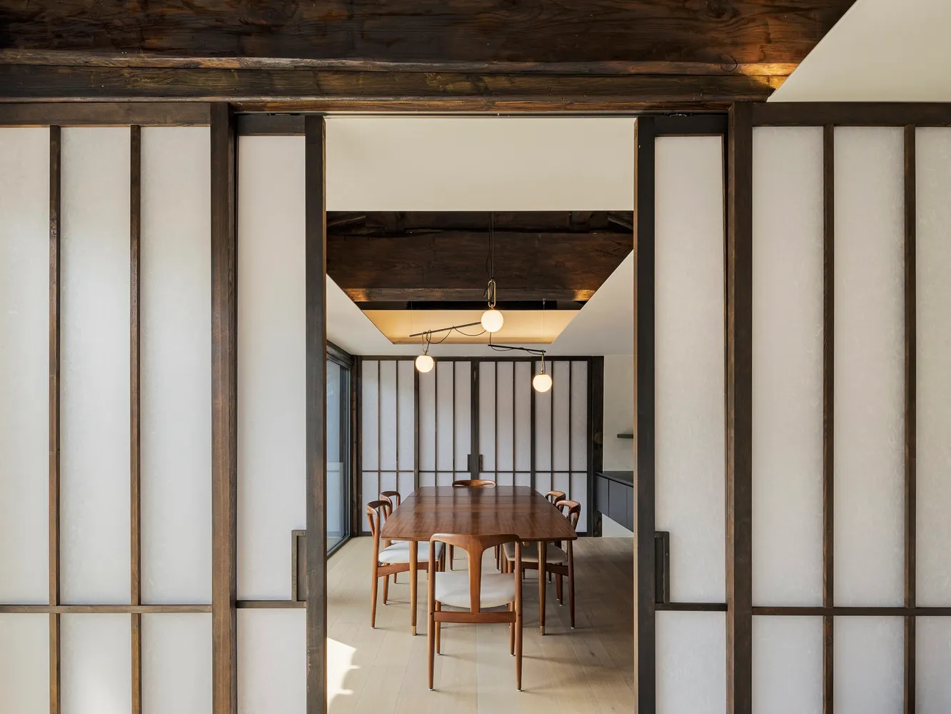 A modern dining room with wooden sliding doors and a wooden dining table surrounded by chairs. The room features a minimalist