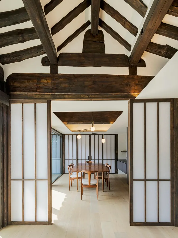 A modern dining room with wooden beams on the ceiling, featuring a wooden table and chairs.