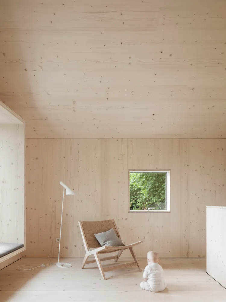 Modern minimalist living room with a wooden floor, white floor lamp, and small window overlooking greenery.