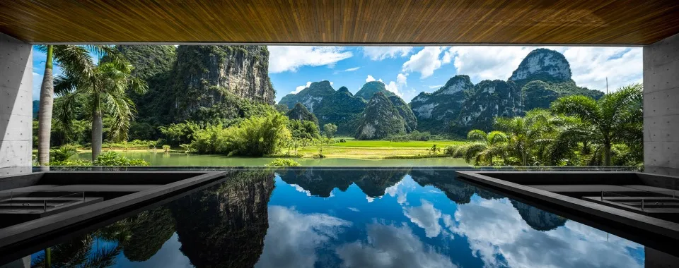 A modern swimming pool with a wooden ceiling and glass walls reflecting the surrounding landscape.