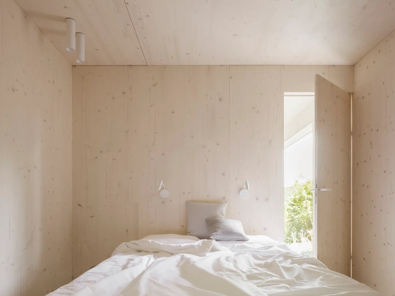 A minimalist bedroom with wooden walls and a bed.