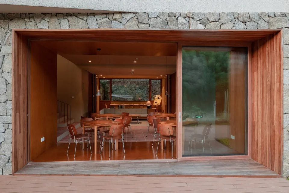 Modern restaurant interior with wooden tables and glass windows overlooking green landscape.