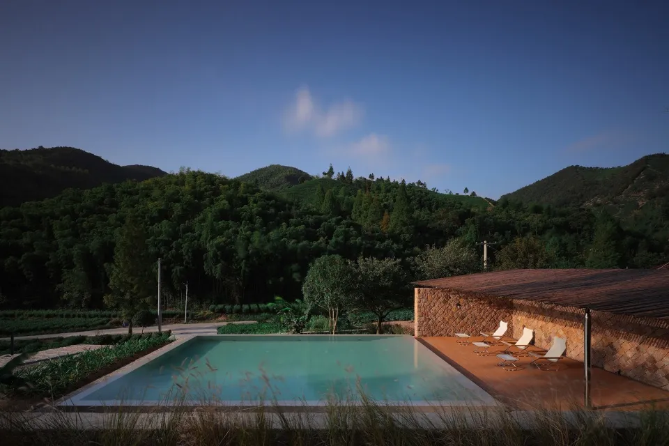 A serene pool area in a natural landscape setting with hills, trees, and a clear blue sky above.