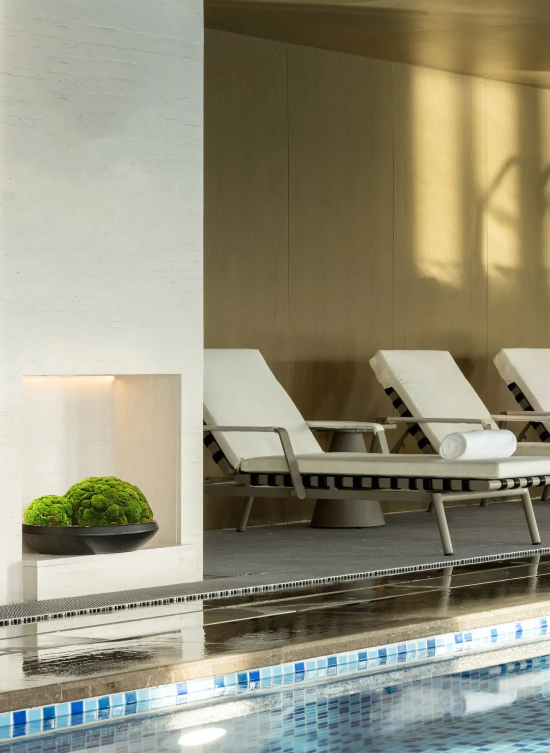 An elegant modern spa area featuring tiled poolside loungers and a wooden wall.