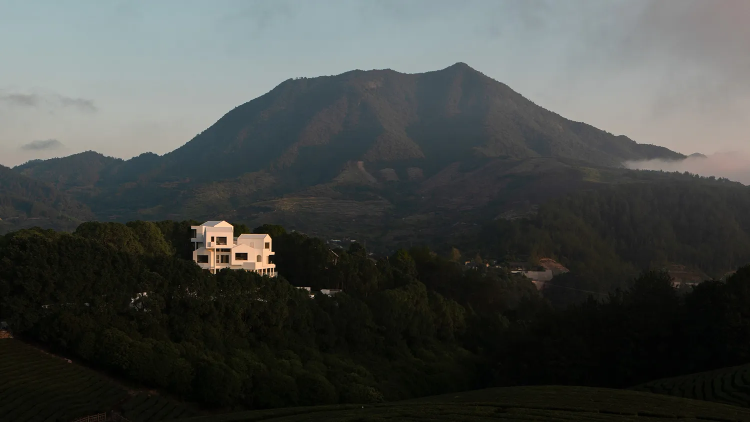 寧靜的山景,前景有一棟顯眼的白色建築,周圍環繞著茂密的綠意與起伏的丘陵。