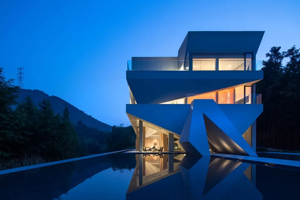 Modern house with a concrete exterior at night with a pool and surrounding trees.