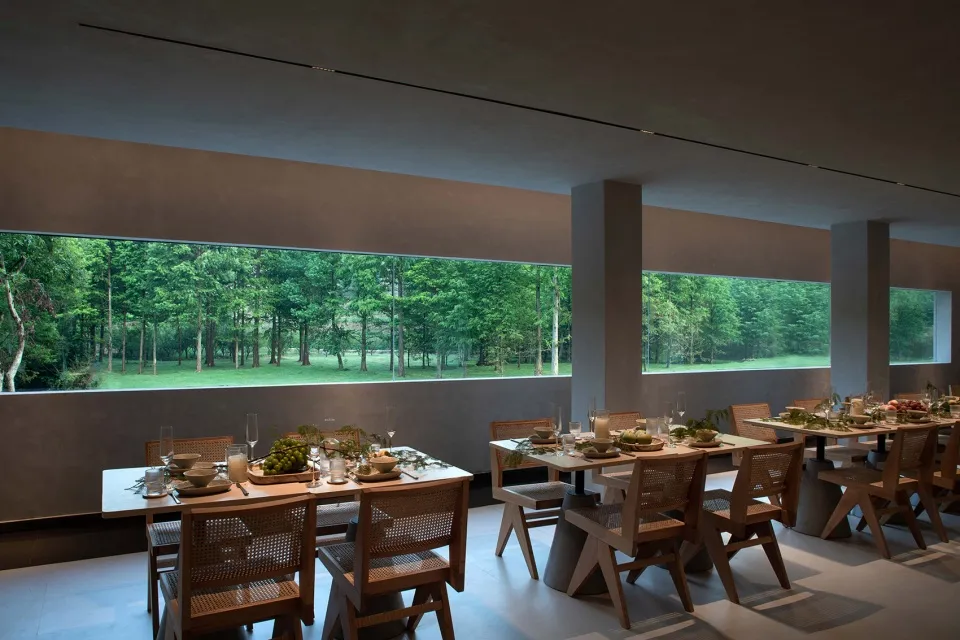 工業風餐廳內擺放木製餐桌椅,旁有大型玻璃窗可眺望窗外綠意。