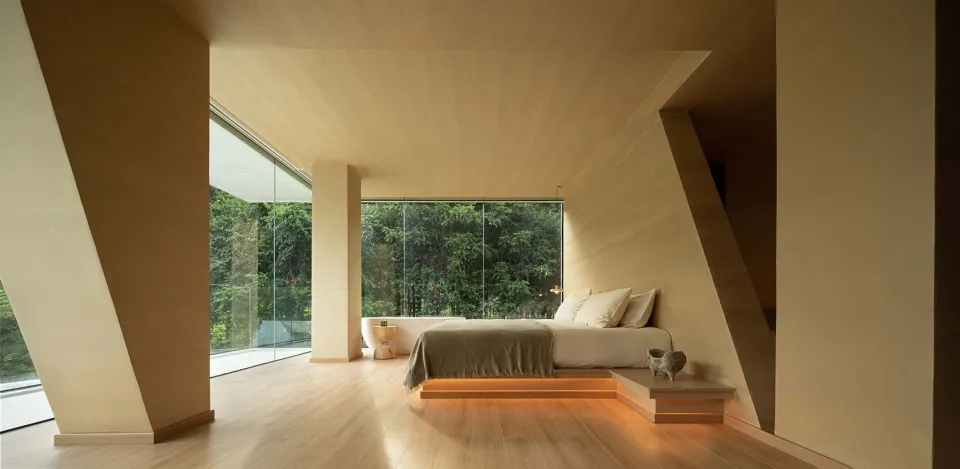 A minimalist bedroom featuring a wooden platform bed with large windows showcasing a natural outdoor view.
