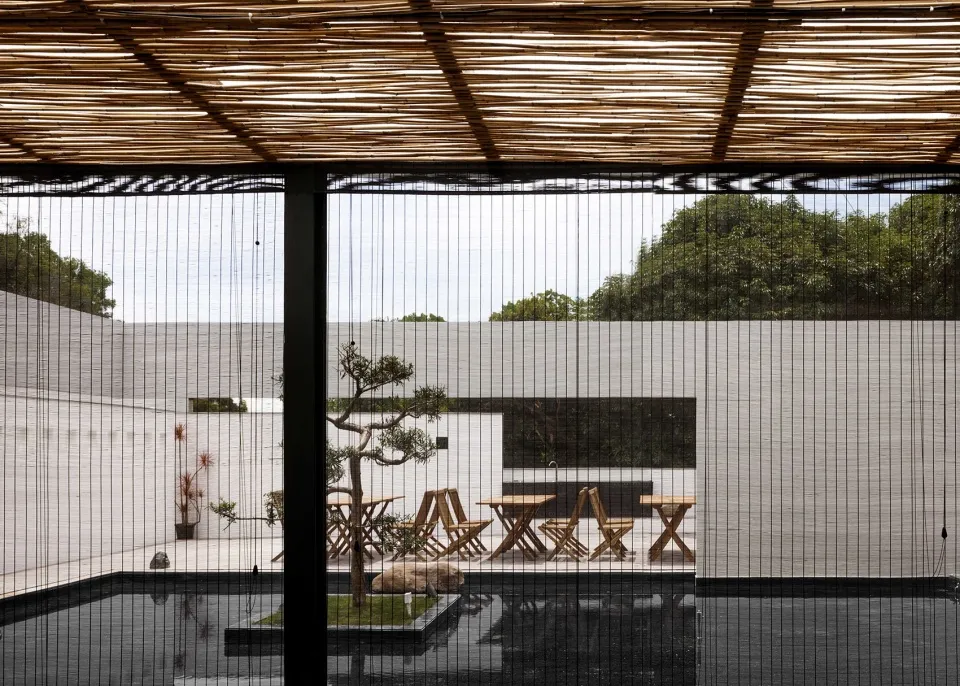 A minimalist terrace with wooden tables and chairs surrounded by greenery.