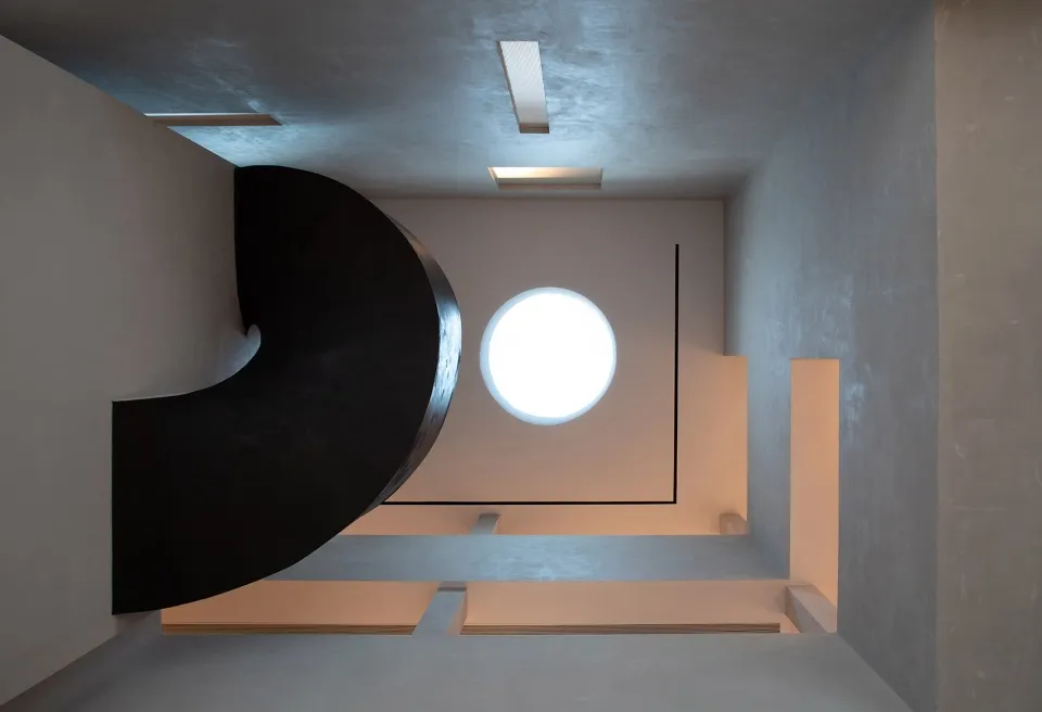 A minimalist, industrial-style spiral staircase made of black metal and concrete interiors with a circular window.