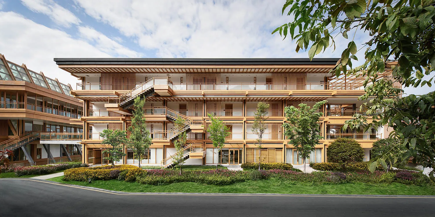 A multi-story residential building with wooden frames and glass panels surrounded by greenery.
