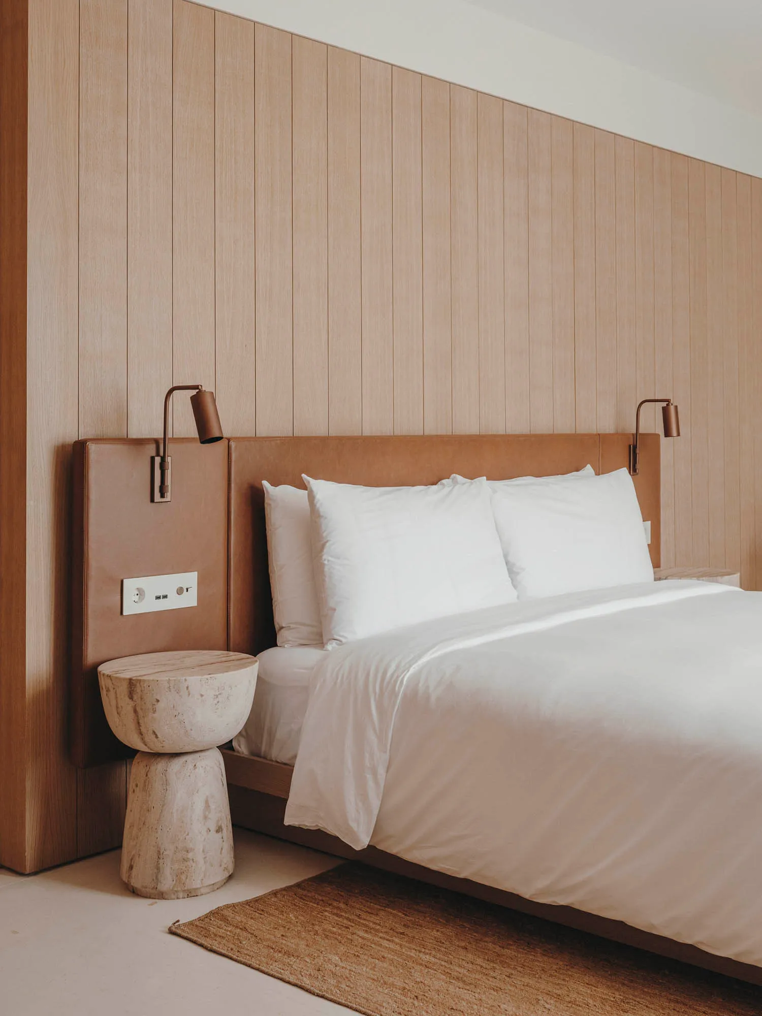 Minimalist bedroom with wooden walls, white bedding, and textured side table.