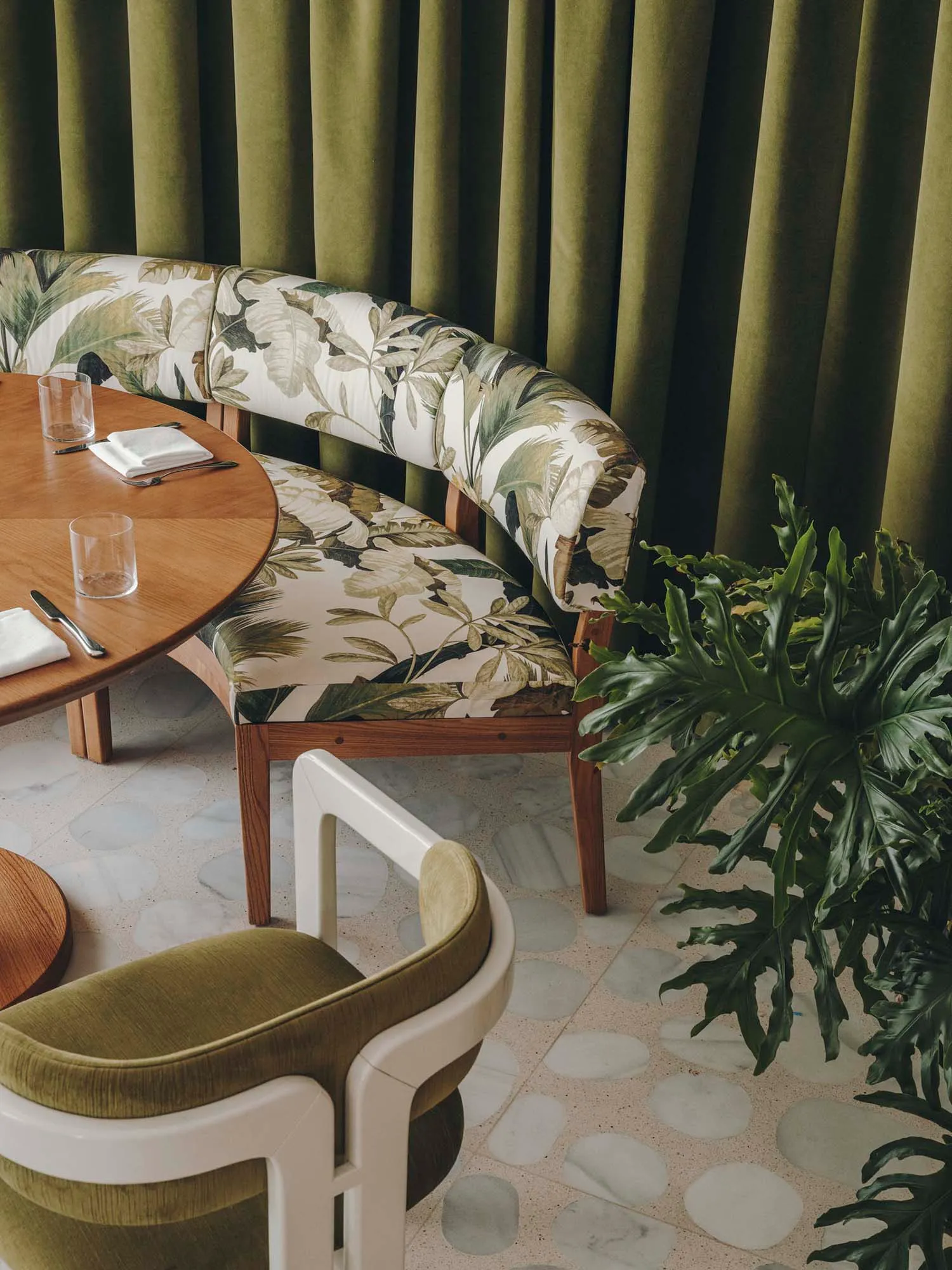 Modern restaurant interior with terrazzo tiles and green curtains.