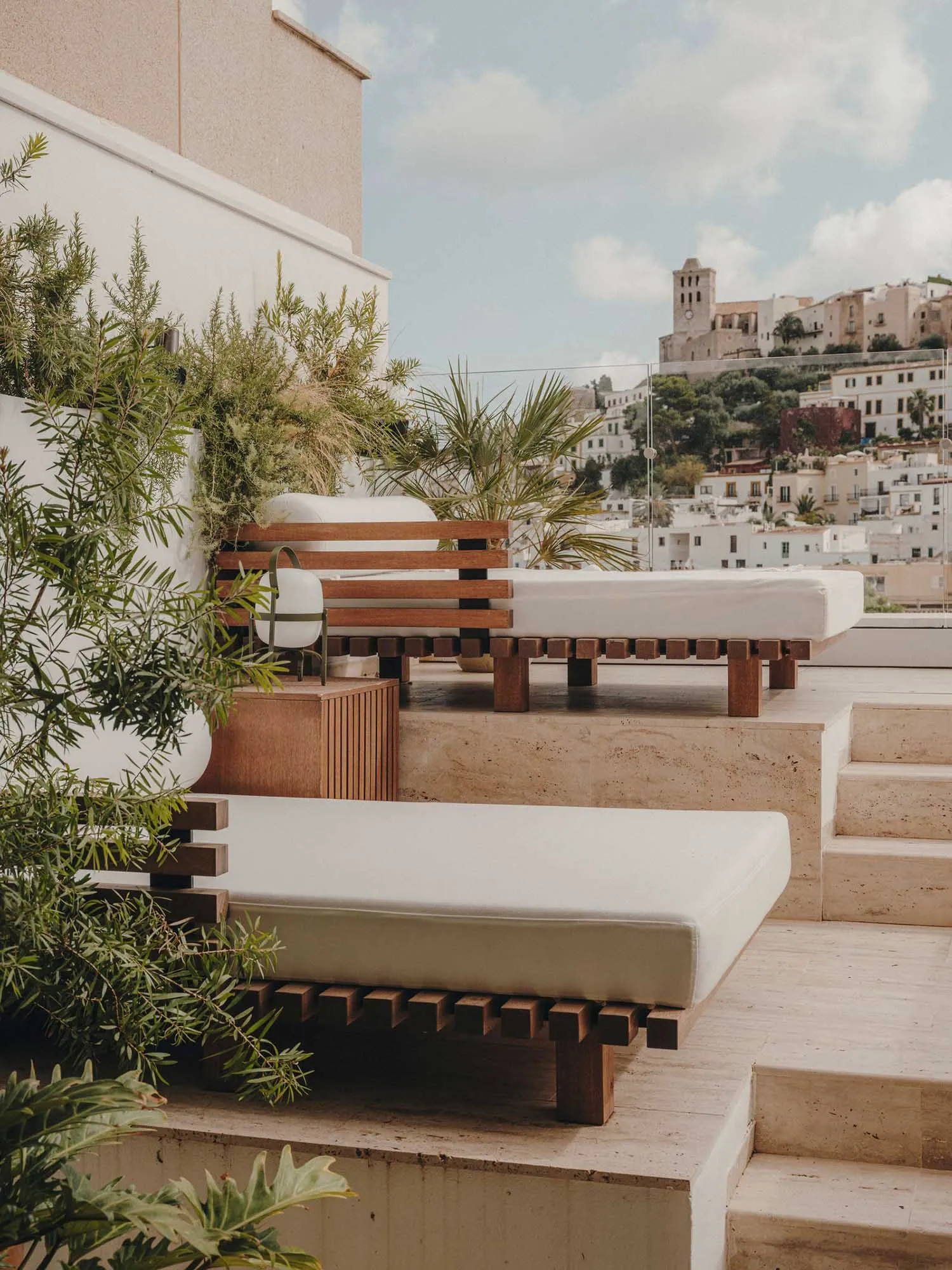 Modern minimalist outdoor rooftop lounge area with wooden benches and white cushions, overlooking a quaint European town on a