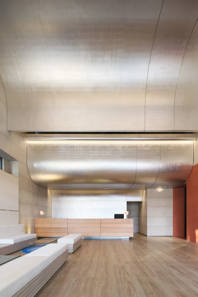 Modern office lobby with metallic ceiling, wooden flooring, and reception desk.