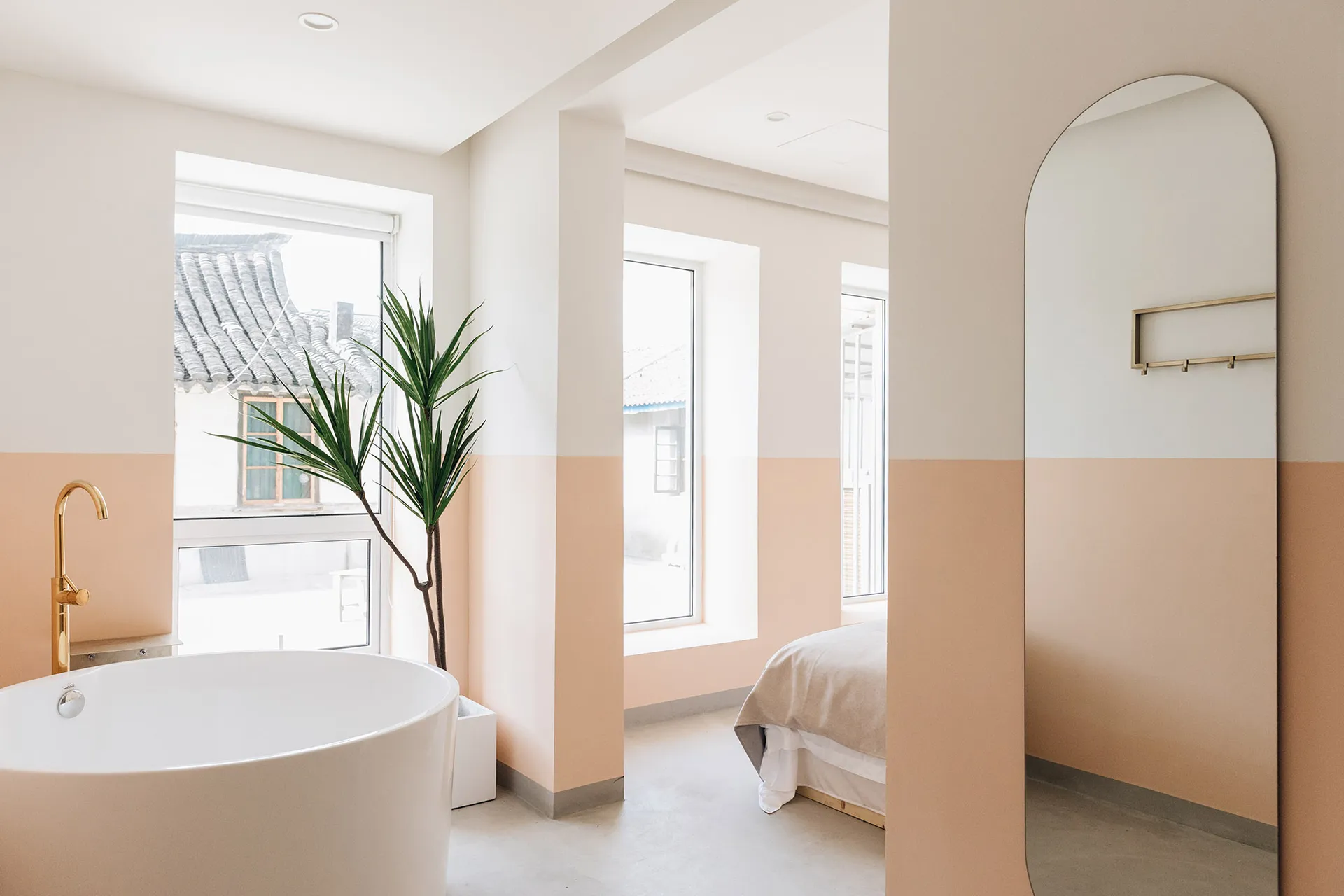 A minimalist residential bathroom with a gold faucet, white bathtub, and peach-colored walls.