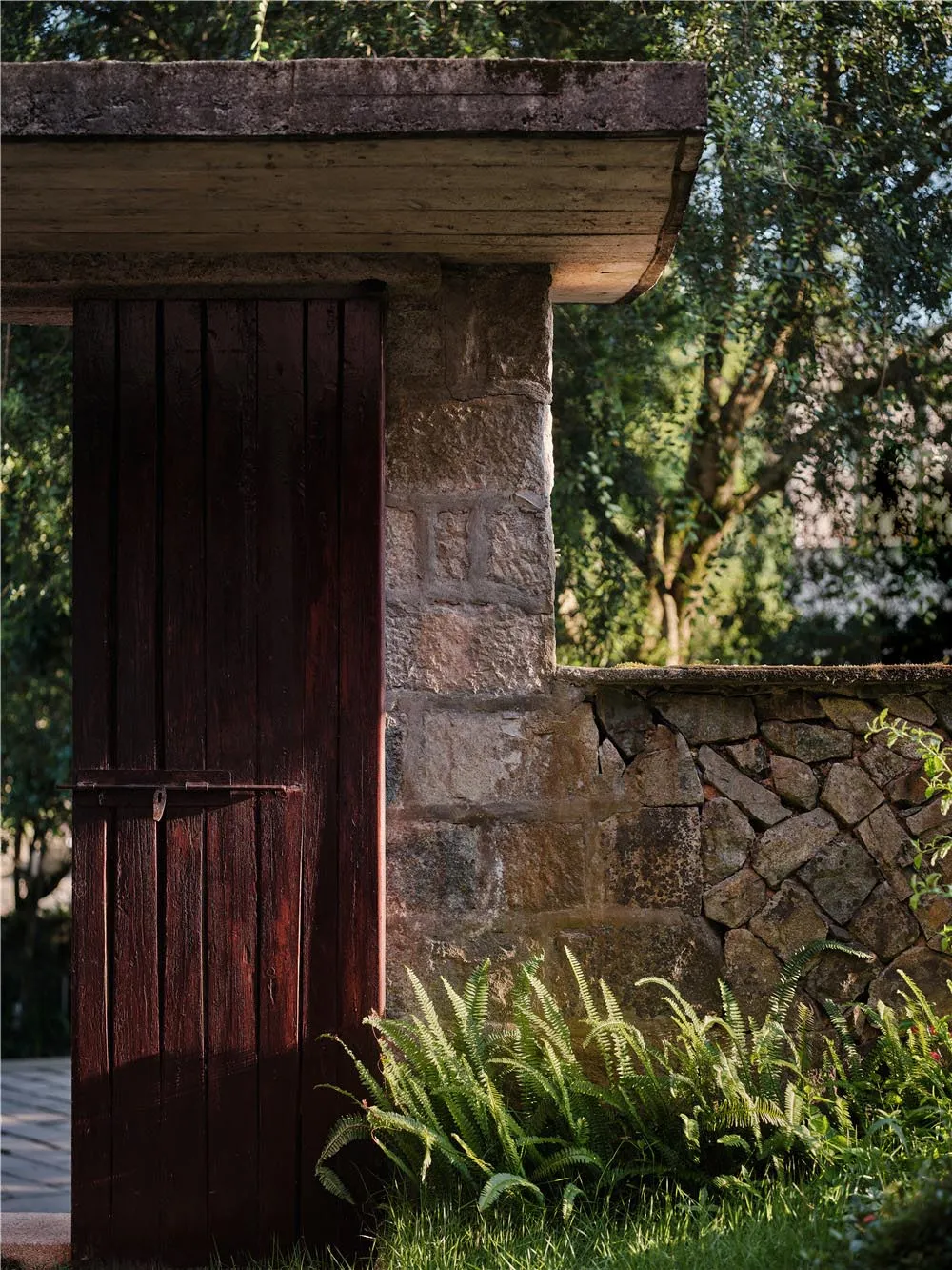 A rustic wooden door with a stone frame surrounded by lush greenery and stone walls.