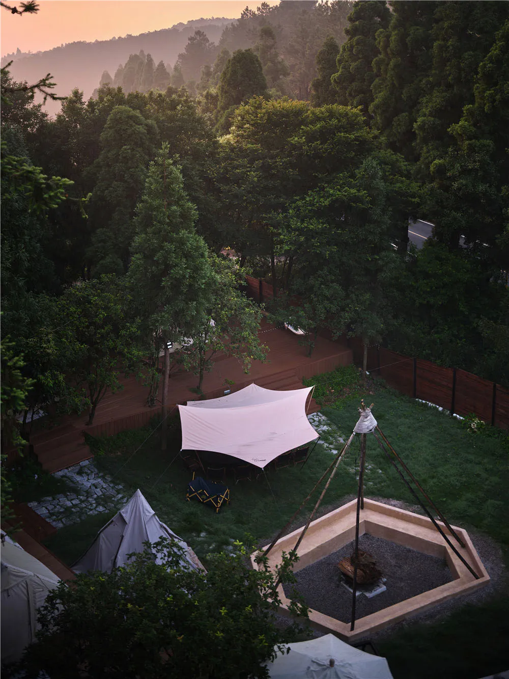 A campsite with tents and outdoor seating set up under a large awning in a forested area.