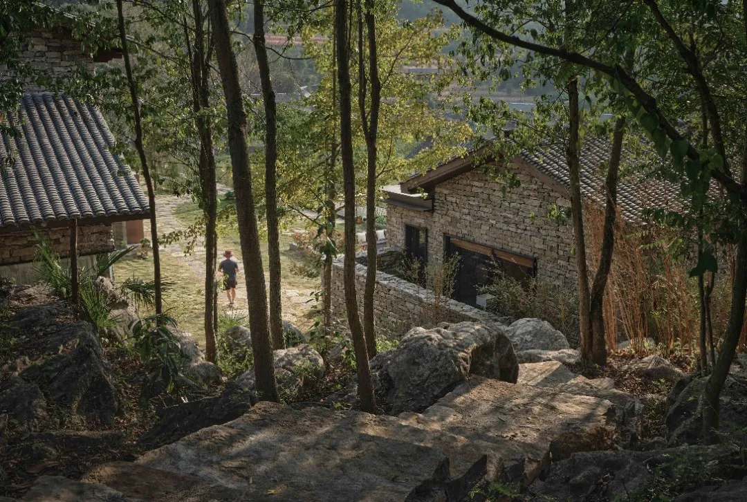 A stone-clad structure in a natural landscape with trees and rocks.