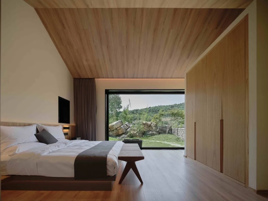 A modern minimalist bedroom with a focus on a wooden ceiling and floor, featuring a large window overlooking a natural landsc