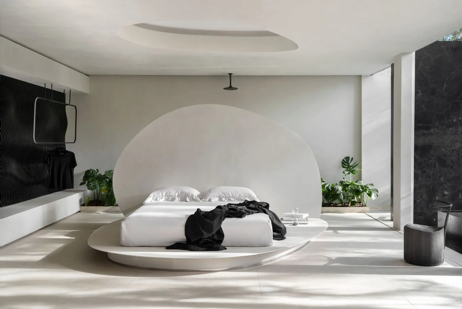 A minimalist bedroom with a concrete platform bed, white bedding, and black accents.