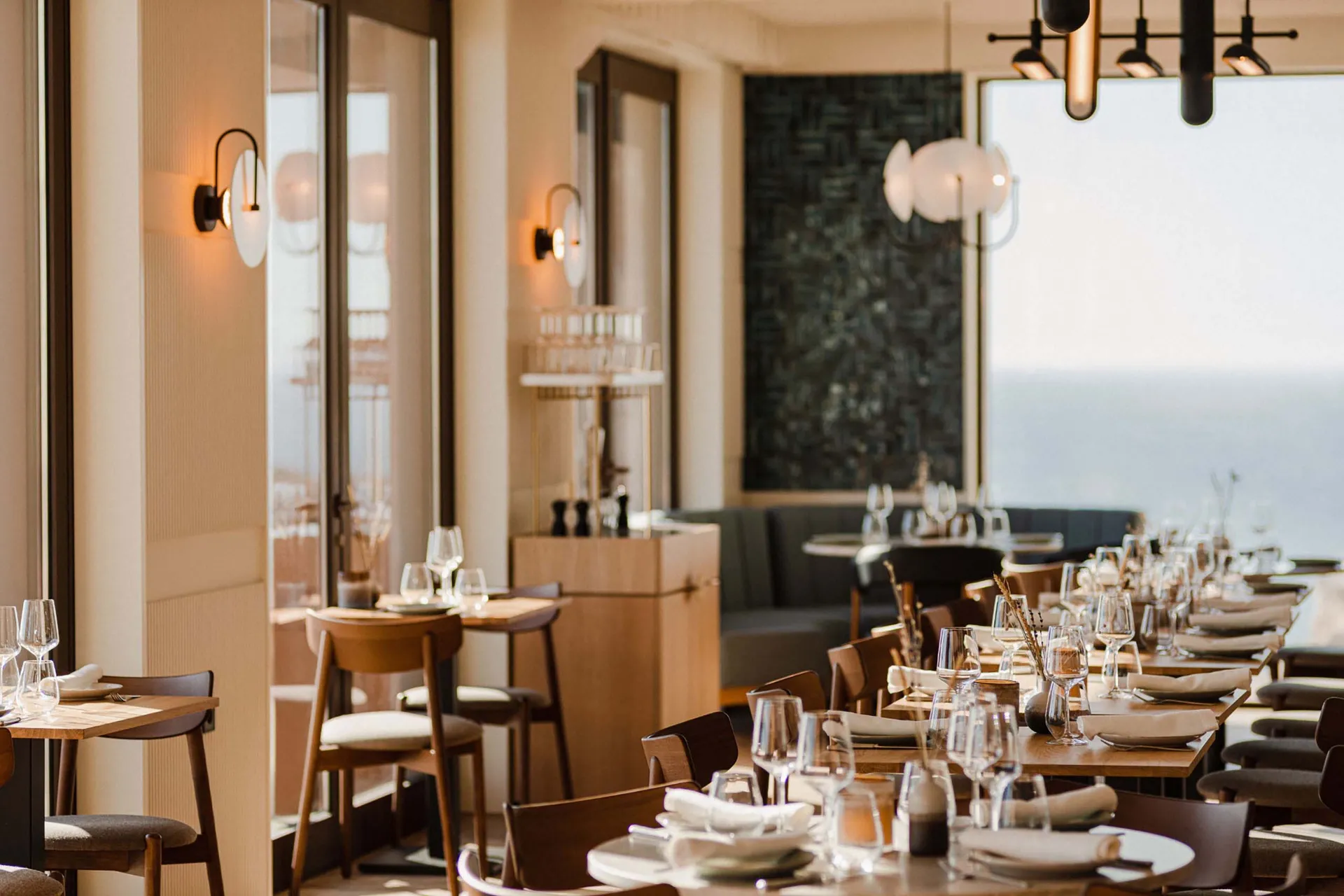 A beautifully designed coastal fine dining restaurant interior with wooden furniture, glass elements, and elegant lighting.
