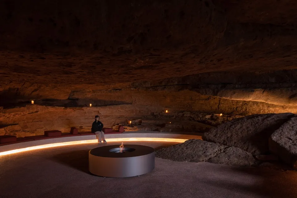 Person sitting on concrete seating area in a cave with rock formations and ambient lighting.