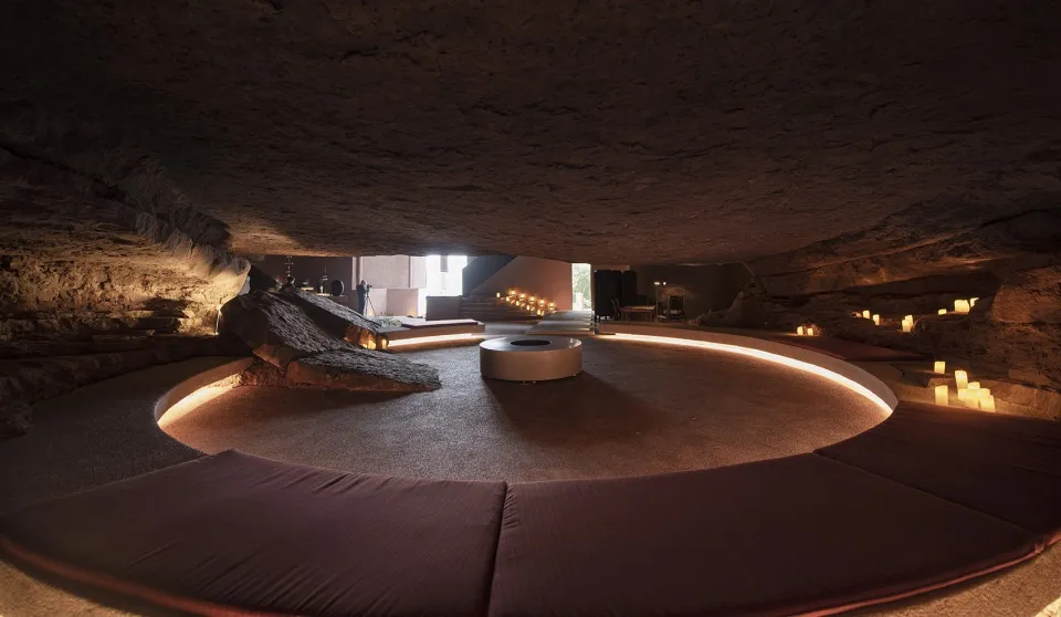 Circular space with industrial design elements, including exposed ceiling and rock formations, illuminated by warm lighting a