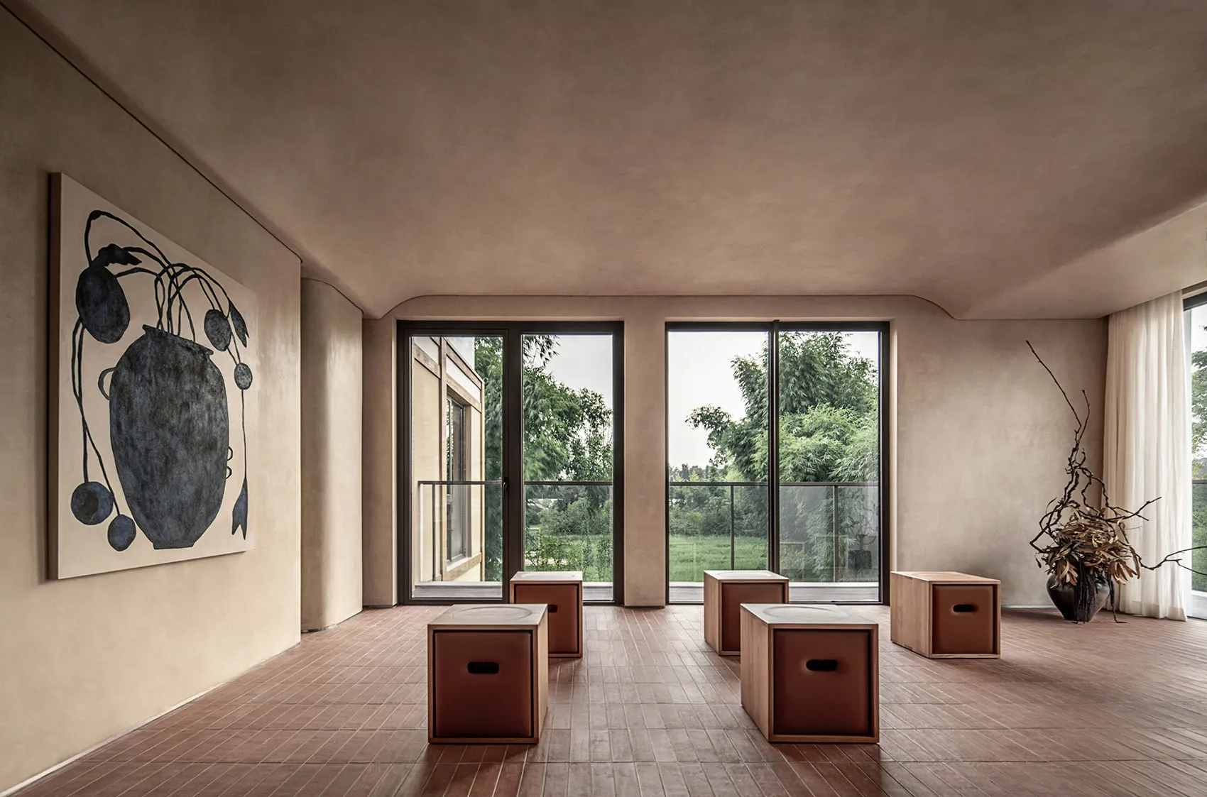 A minimalist living room features clay-tiled flooring, large windows, and a simple, modern decor.