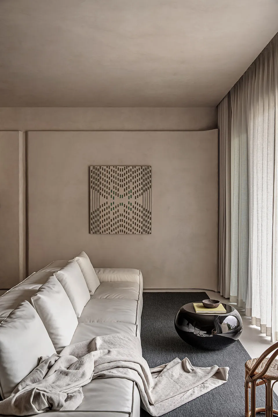 A modern minimalist living room featuring a white sofa with cushions, a black round coffee table, and a geometric wall art pi