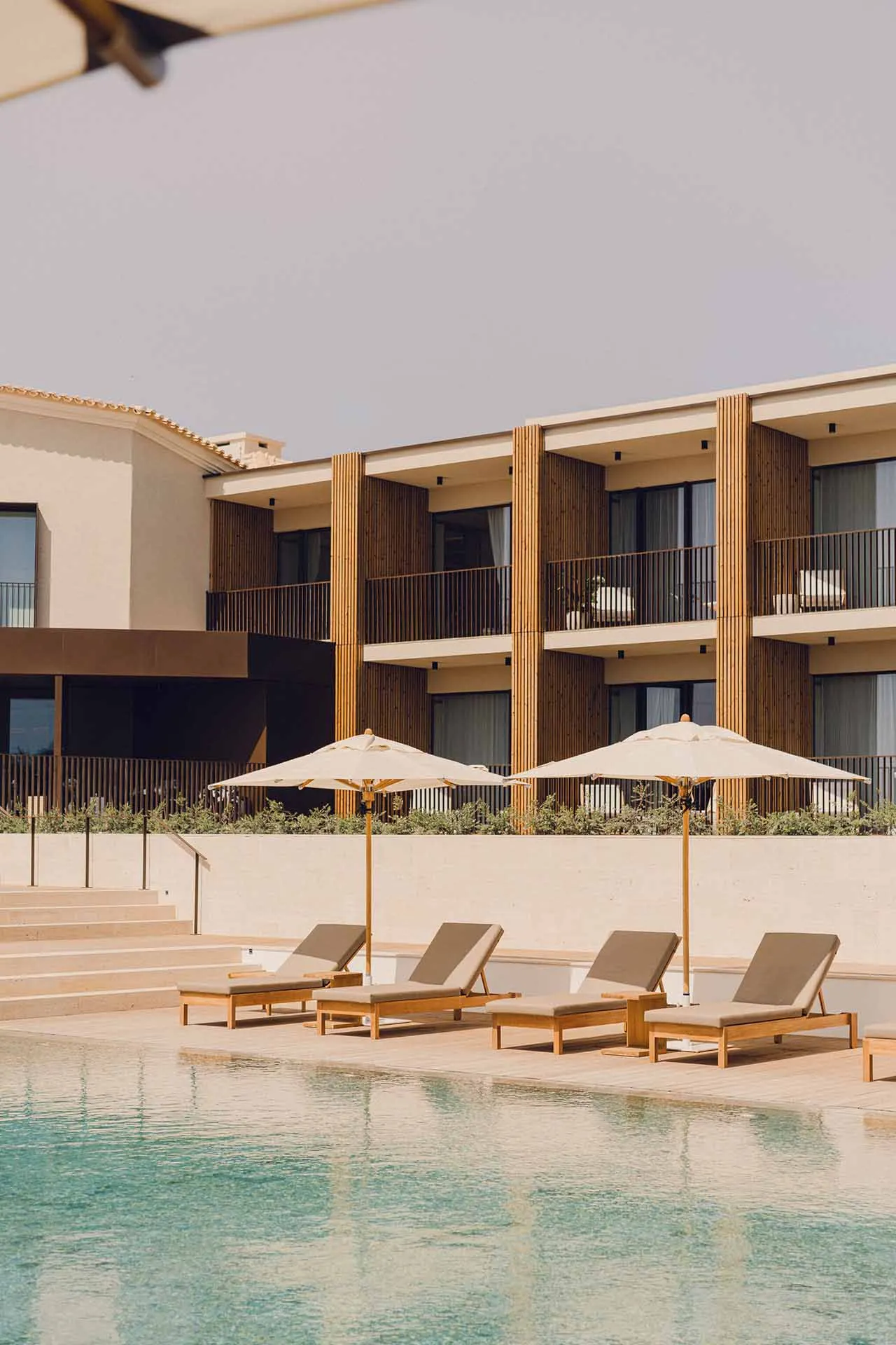 Swimming pool area featuring modern residential architecture with wooden sun loungers, concrete steps, and lush greenery.